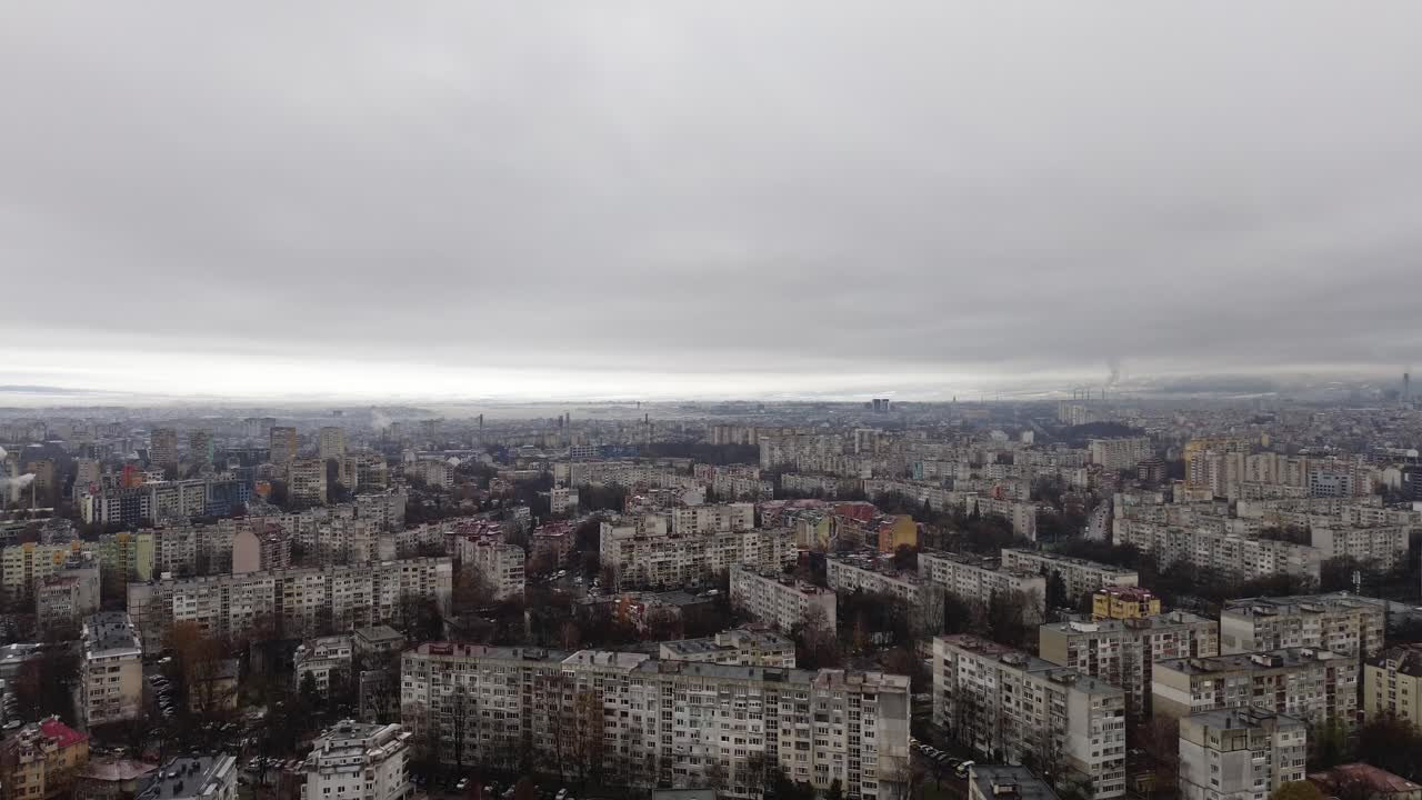 Drone footage descending towards old communist-era apartment blocks in Sofia, Bulgaria, on a dark, overcast winter day. The scene is wet, dreary, and leafless trees fill the urban landscape.