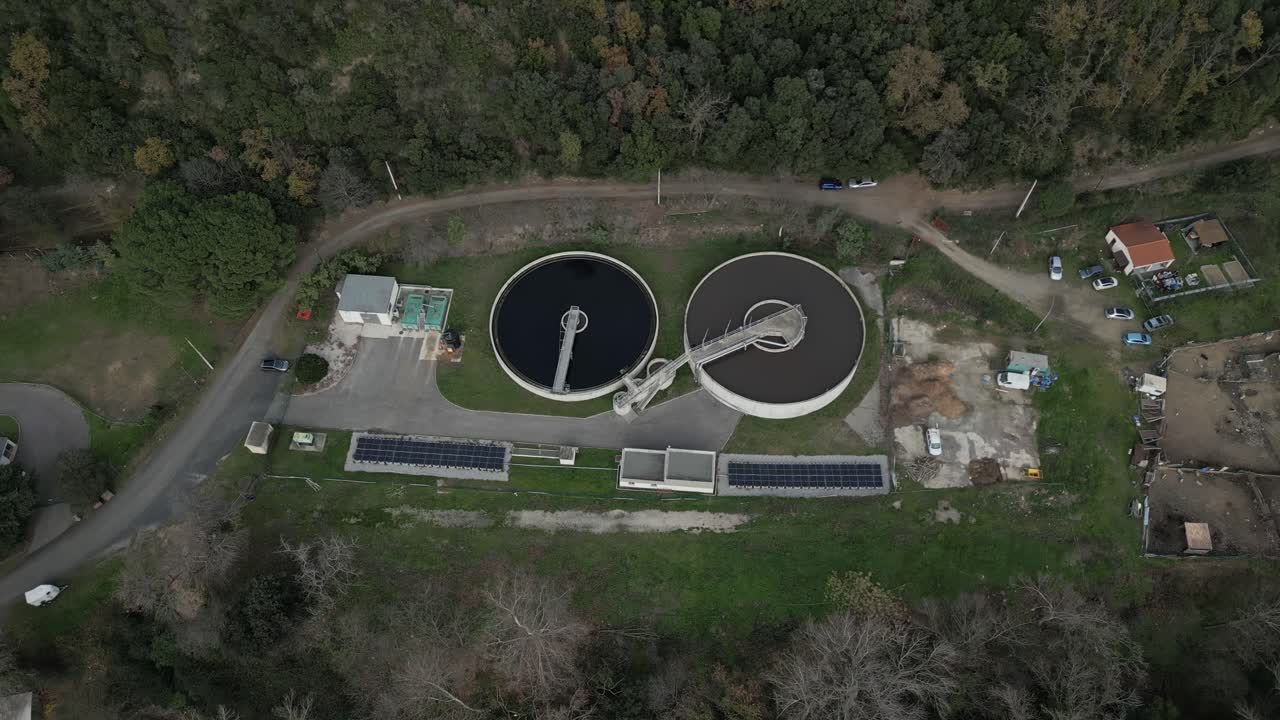 High angle view of a water treatment plant near amelie les bains, france, featuring circular filtration tanks, solar panels, and surrounding woodland