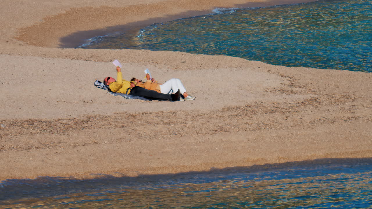 Nice, France - February 10, 2025: A man and a woman reading, lying on the beach