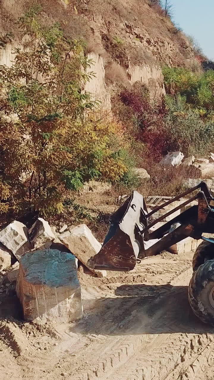 specially machinery with a bucket for picking stones is working in a quarry near the hill with forest. Close-up. Vertical video