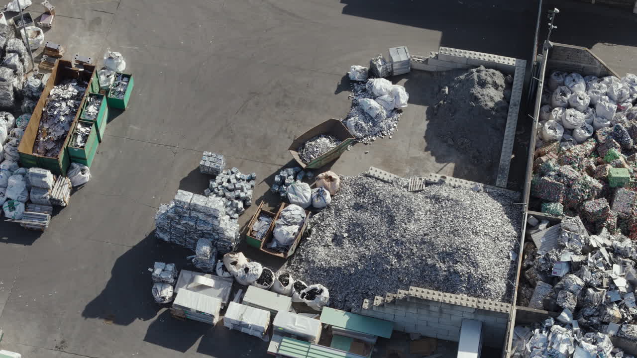 Drone perspective of a recycling yard with large piles of scrap metal and heavy machinery in action