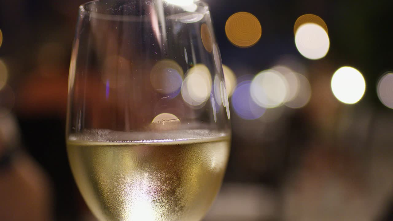 Primo piano di un calice di vino bianco ghiacciato, luci bokeh, cena elegante, messa a fuoco selettiva, ripresa stabile