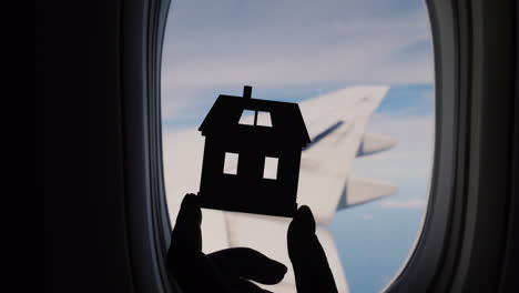 sosteniendo la figurilla de la casa junto a la ventana del avión