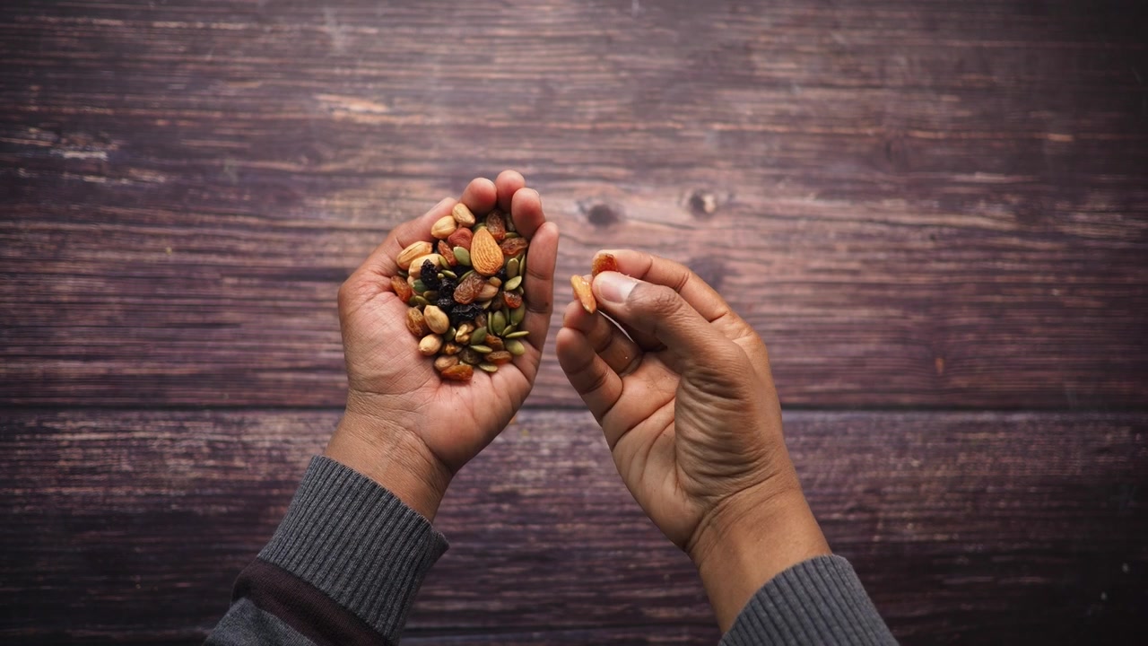 Top View of Hands Sorting a Mix of Nuts and Dried Fruits