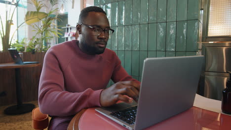 young black man working remotely on laptop in cafe