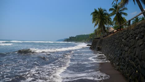 full shot, wave hitting the walls of the bitcoin beach on a bright sunday in el salvador, mexico, palm trees and bright blue sky in the background