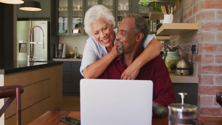 Älterer afroamerikanischer Ehemann und Ehefrau gemischter Herkunft arbeiten glücklich am Laptop zu Hause.