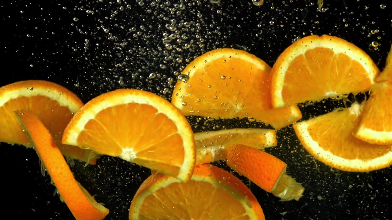 Leuchtende Orangenscheiben und -schalen schweben in sprudelndem Wasser.