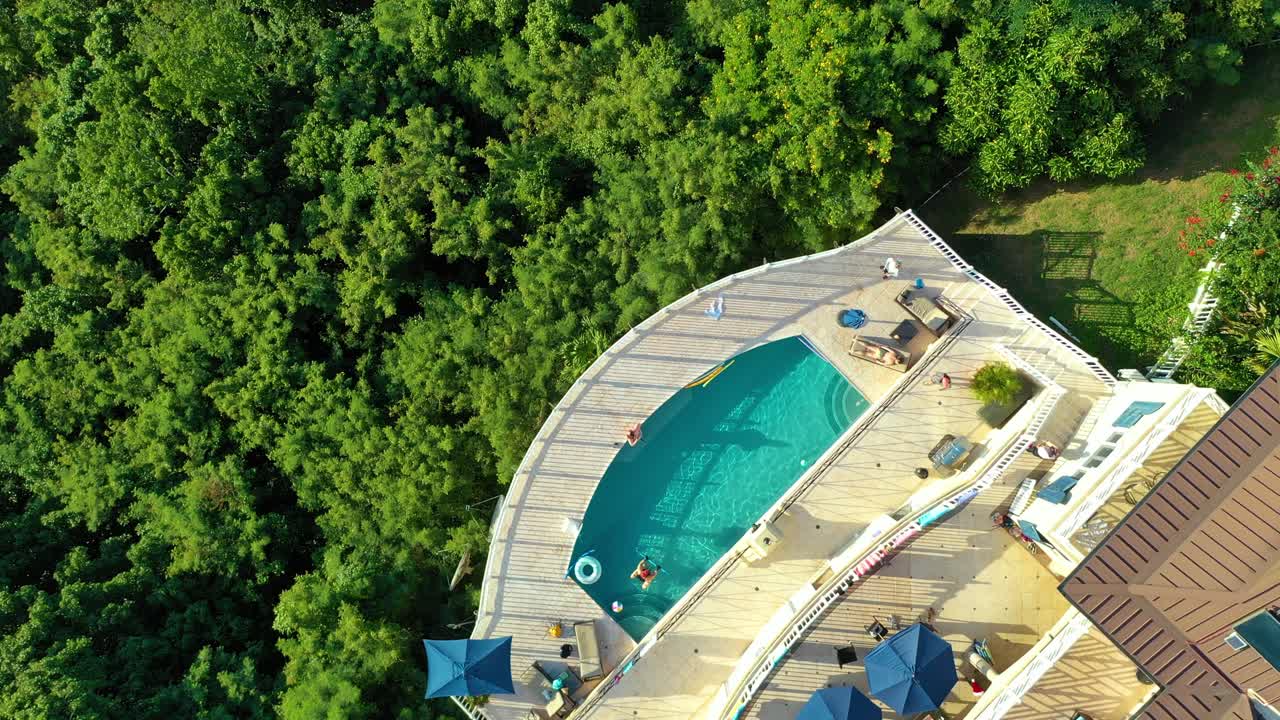 Flying over St. Croix by drone reveals scattered upscale homes set into rolling forest hills, surrounded by island jungle and distant misty mountains glowing in the bright midday Caribbean sun