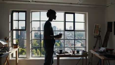 man drinking a beverage by a large window overlooking a city skyline
