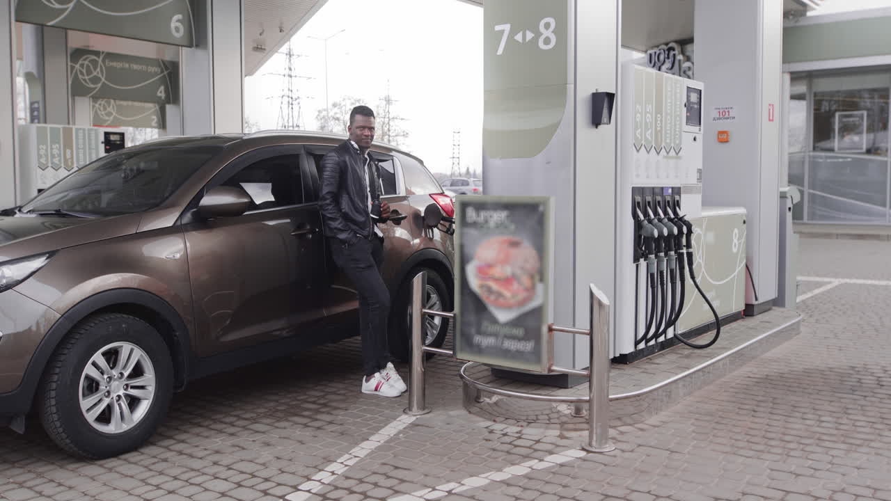 Giovane uomo d'affari africano concentrato, con giubbotto di pelle nero, beve il suo caffè da asporto mentre è in piedi