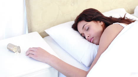 woman sleeping in bed by spilt bottle of pills on table