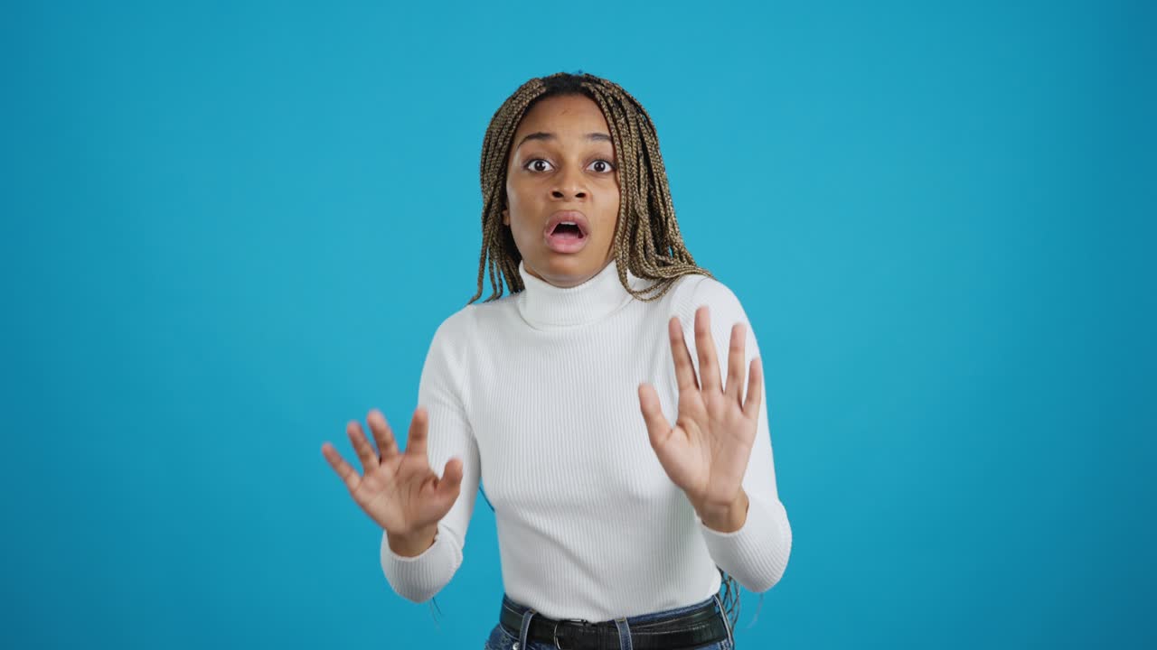 Scared Young African American Woman Raising Hands in Defense on Blue Background
