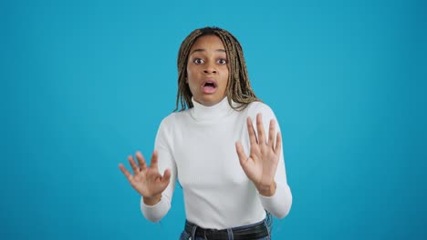 scared young african american woman raising hands in defense on blue background
