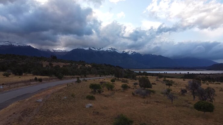 Vista aerea che sorvola una strada con traffico di auto e maestose cime montuose coperte di neve, ripresa in Patagonia, Argentina, Sud America