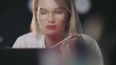 gedachtevolle zakenvrouw op zoek naar laptop in een donker kantoor. vrouw die op de werkplek werkt