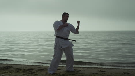 athlete man practicing kicks on beach. strong guy training fighting skills.