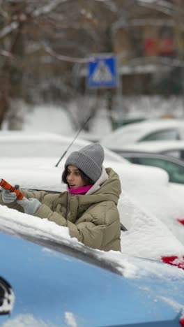 woman removing snow from car in snowy city