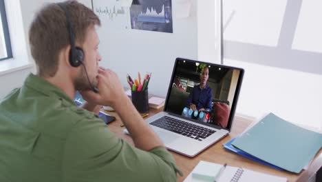 Caucasian-man-using-laptop-and-phone-headset-on-video-call-with-male-colleague