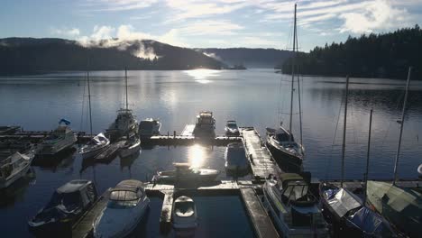 Multiple-sailing-yachts-moored-at-a-wooden-scaffolding-in-a-marina-with-the-Indian-Arm-bay-at-background-on-a-sunny-day