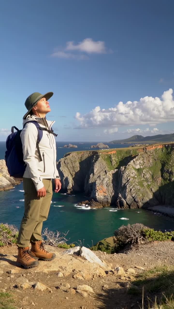 Vertikal video: Pauserende turgåer som vipper hodet oppover og skanner havet på en klippe med hatt, sekk, kopieringsområde