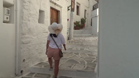 una chica vestida de senderismo con sombrero de verano caminando por un estrecho callejón griego revela