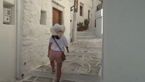 girl in hiking outfit with summer hat walking through narrow greek alley reveal