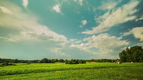 static shot of mystic white clouds flying over green field with hay bales in timelapse at daytime