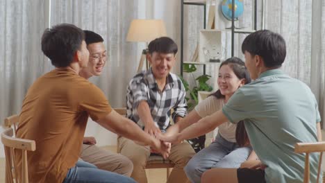 아시안 십대 그룹은 의자에 앉아서 집에서 토론하는 원을 형성합니다. 팀워크의 상징으로 손을 함께 넣고, 비명을 지르며 축하합니다.