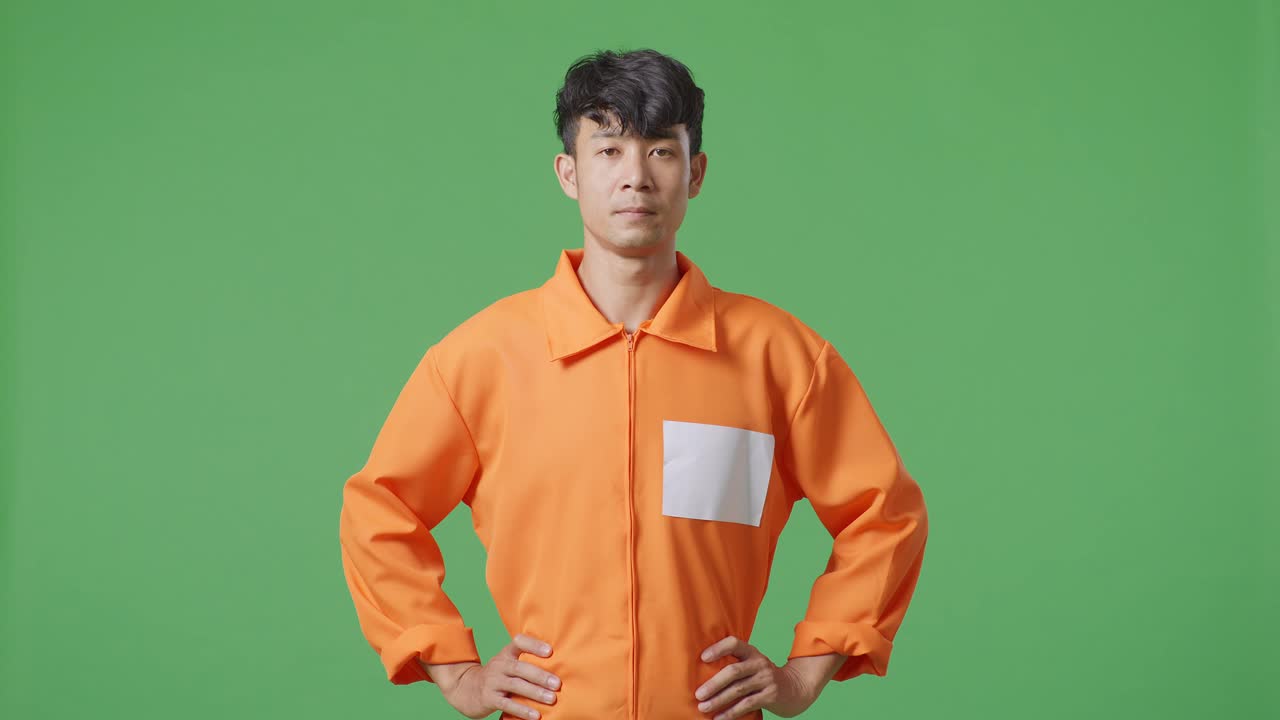 녹색 스크린 배경에 팔을 들고 서 있는 아시아 남성 수감자, 머리를 들고 카메라를 바라보고