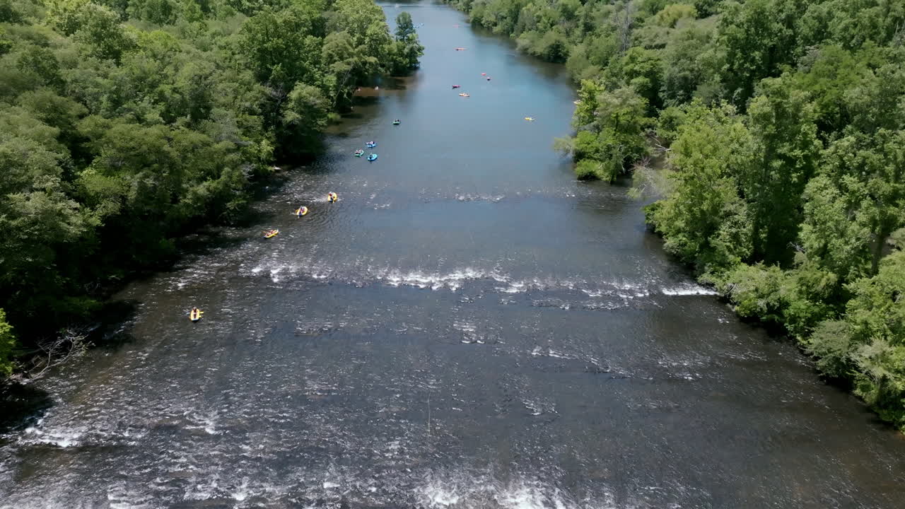 Birds eye aerial drone footage of rapids on the Hiawassee River with people in tubes floating down with lush green forest on either side.