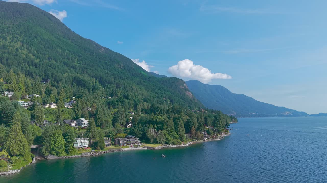 An aerial drone shot of Lions Bay, with luxury homes on the coast beneath Brunswick mountain with Bowyer and Bowen island on the right