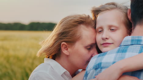 the family hugs their father against the background of wheat which is swayed by the wind