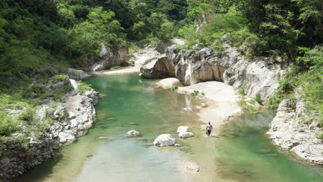 turista cruzando lentamente un río rocoso y poco profundo en una selva tropical mágica