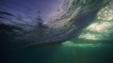 underwater pan up to surfer on single fin longboard as wave breaks