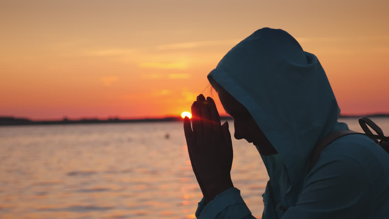 una mujer de mediana edad en una capucha rezando cerca del lago al atardecer