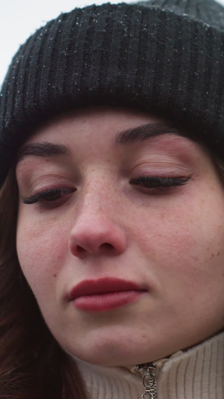 Close up shot of lady in black cap walking with wind-blown hair and thoughtful look against blurred city background during cold quiet day with overcast sky and soft natural winter