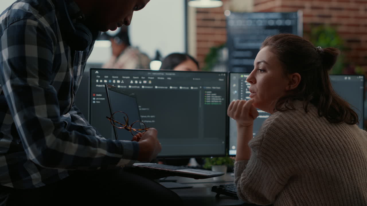 Junior programer sitting down on desk showing laptop with source code to senior dev