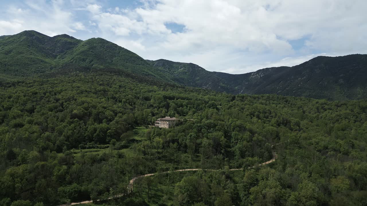 Verdant mountain landscape featuring isolated building nestled amid lush green forest, winding road curving through pristine wilderness with sweeping scenic panorama
