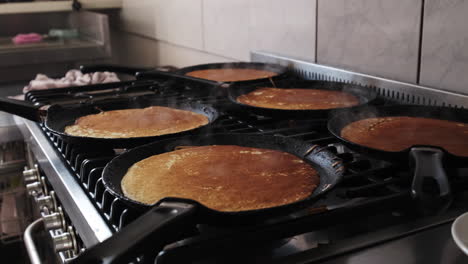 dolly forward on pankakes being cooked on the pans of a gas oven