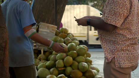 Tender-coconut-water-seller-and-buyer-exchanging-money,-cash,-and-currency-in-the-marketplace-during-a-transaction,-India