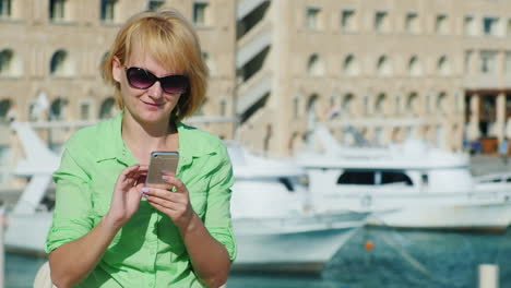 mujer escribiendo sms en el horizonte de una ciudad turística con yates