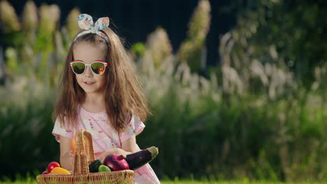 Portrait-of-a-cute-little-girl-with-a-basket-of-vegetables.-Sitting-on-a-green-lawn