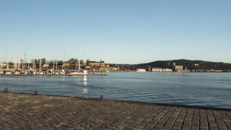 people at oslo harbour at sunset, akershus fortress behind, time lapse wide angle