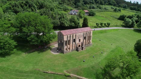 Drone-Volando-Hacia-Atrás-Revelando-La-Antigua-Iglesia-Prerrománica-En-Un-Entorno-Natural-Verde