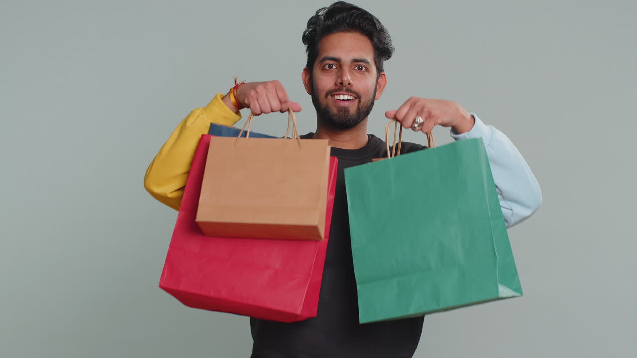 Indian man showing shopping bags advertising discounts amazed with low prices black friday holidays
