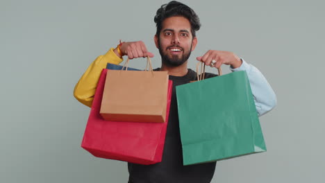 indian man showing shopping bags advertising discounts amazed with low prices black friday holidays