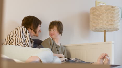 young girl with down syndrome reading magazine and her mother is kissing her