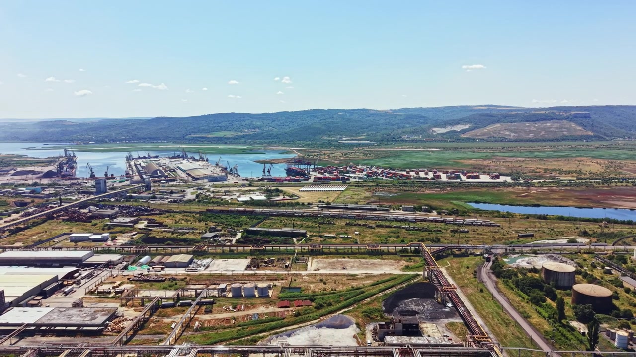 Utsikt over et stort industriområde nær vannet med fraktcontainere og utstyr på en klar dag i landlige omgivelser med fjell i bakgrunnen