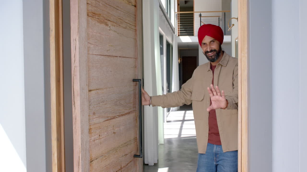Welcoming guests, man in turban smiling and opening front door of home